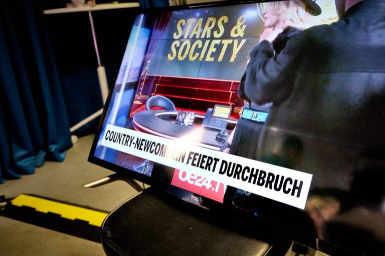 Fernsehbildschirm mit Country-News und Talkshow-Szene.