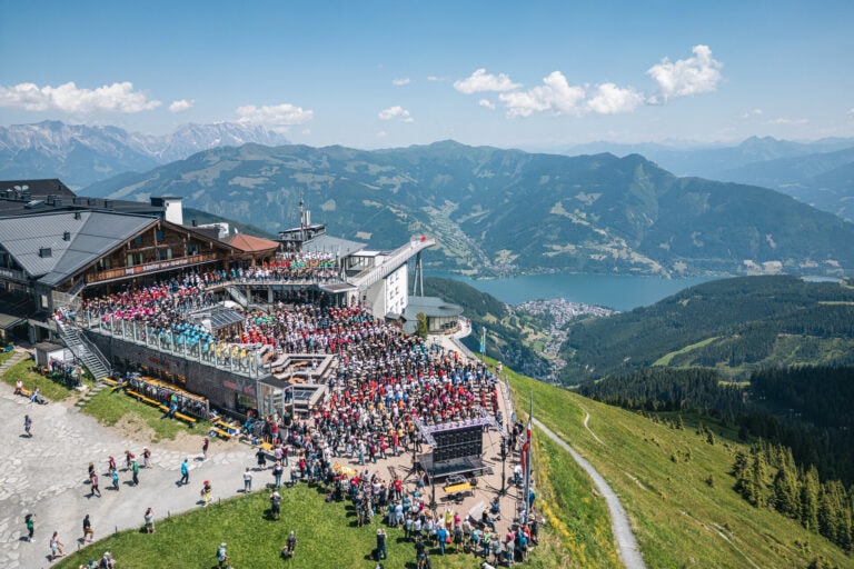 Große Menschenmenge feiert auf einem Bergrestaurant mit Seeblick.